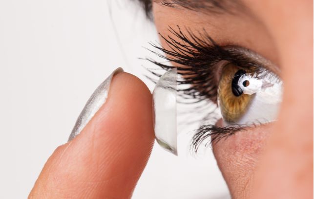 Close up of women with green eye putting in contact lenses into eye