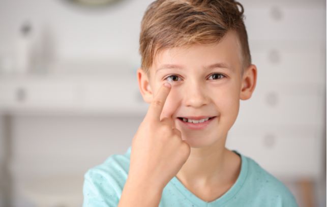 Young boy holding contact lens on finger before putting in eyes to help control myopia