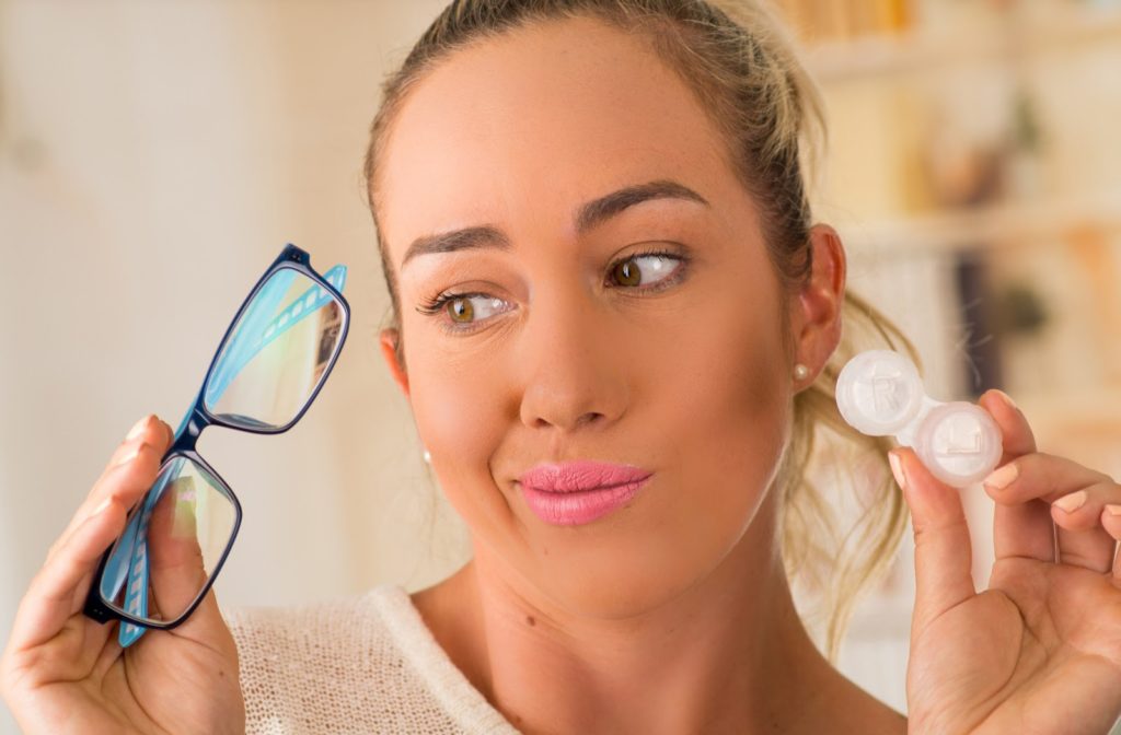 Women holding a pair of glasses and contact lenses in the other thinking about her options