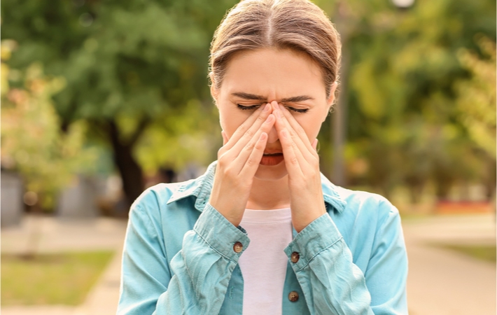 Alt text: A woman rubs the inside of her eyes from allergies as she's out for a walk.