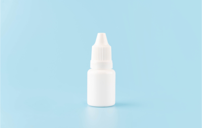 Alt text: An unbranded bottle of eye drops against a light blue background. 