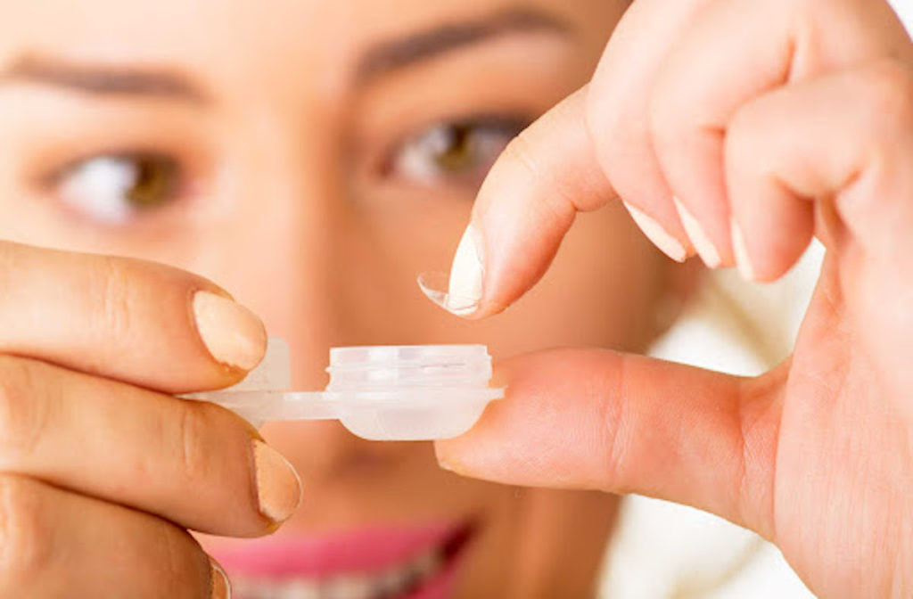 A woman is placing her contact lens back into the contact lens case.