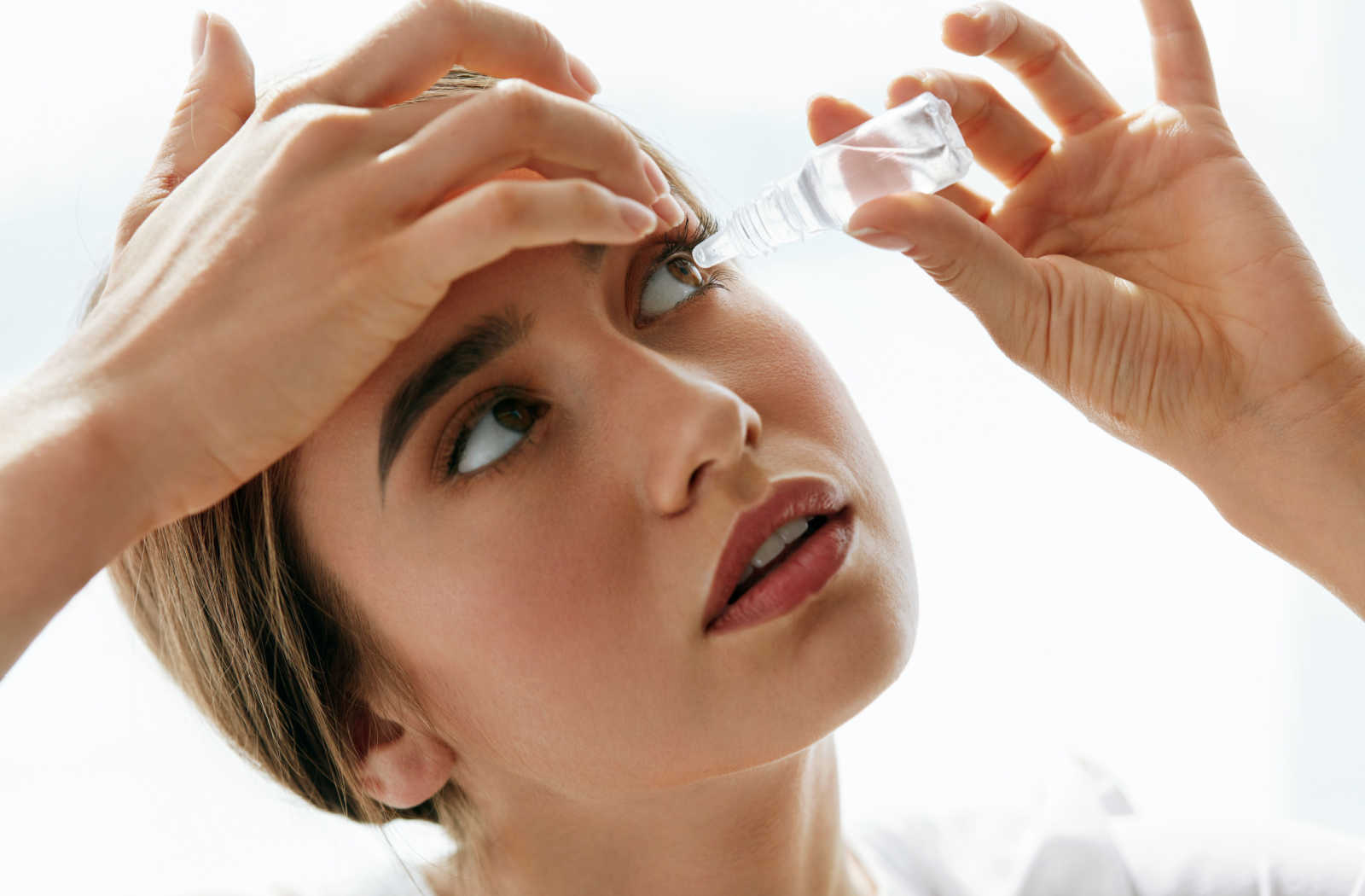 Woman putting eyedrops into her left eye.