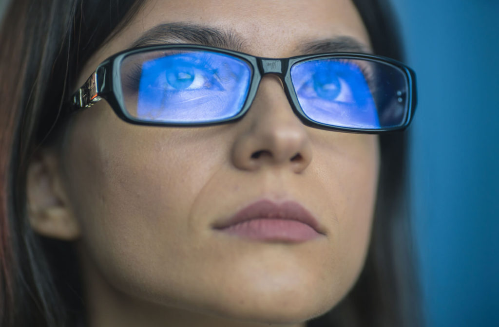 Suggested edit: "A woman with blue light reflected on her glasses from a screen."