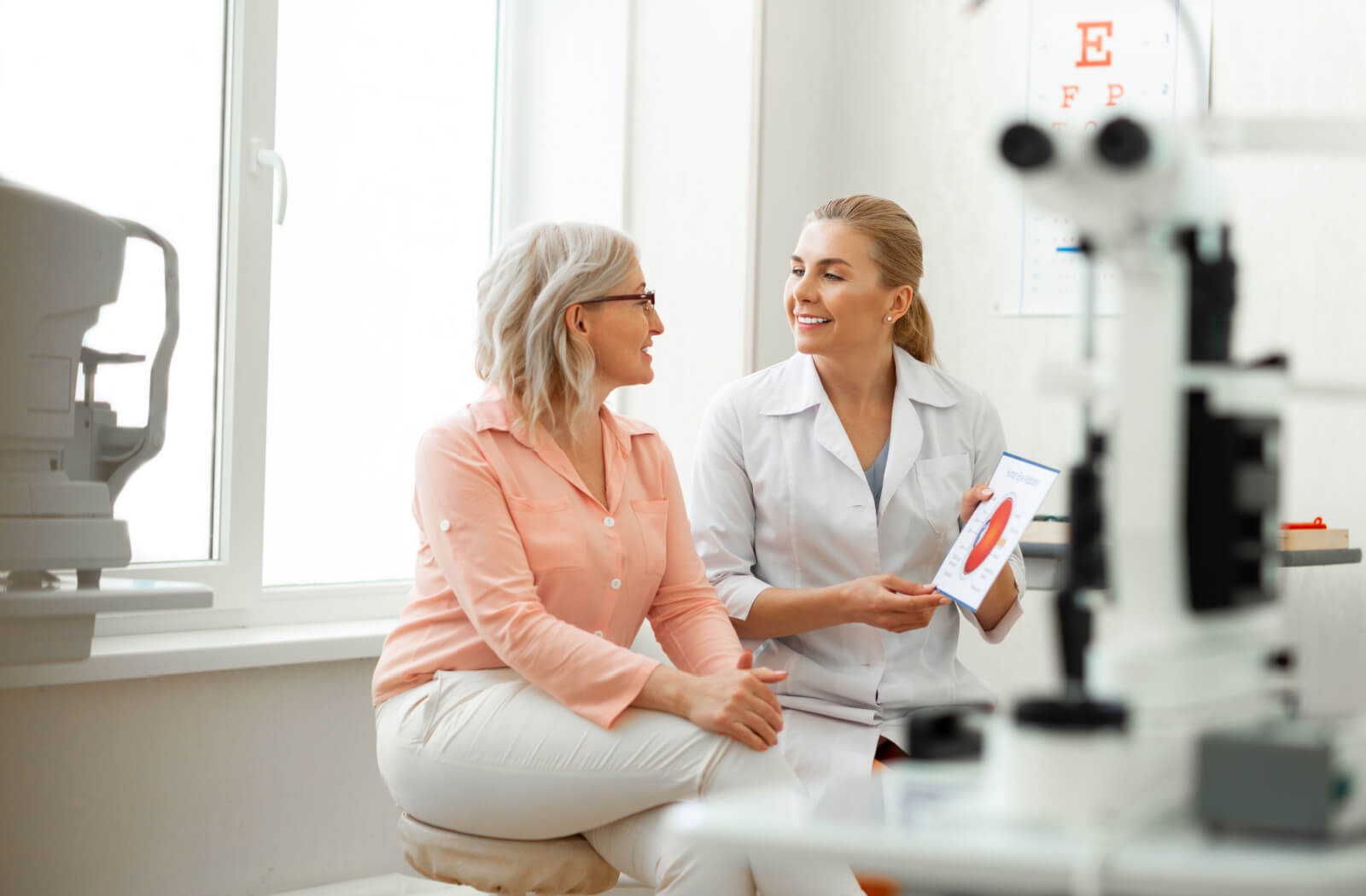 A woman sitting in an optometrist's office and smiling at her eye doctor.
