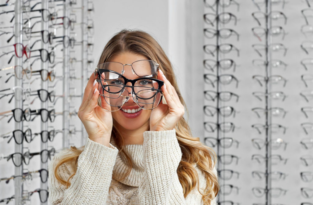 A young woman at the optical shop is choosing glasses that fits her face.