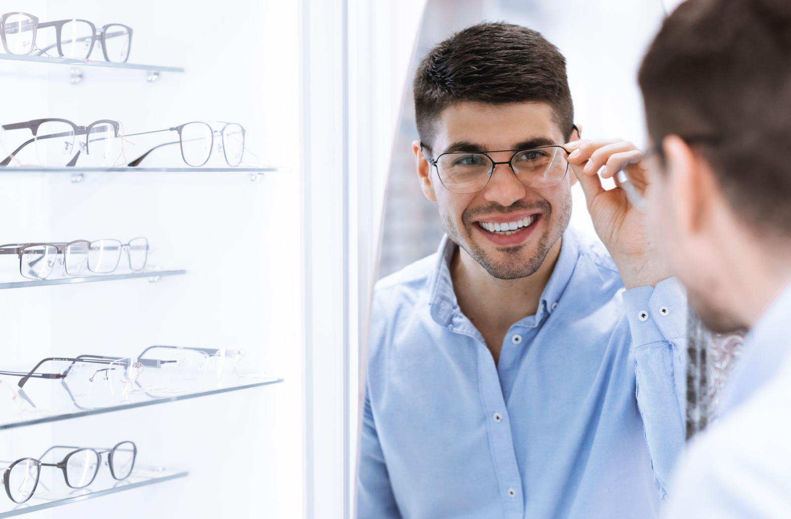 An adult man is trying new eyeglasses in front of a mirror in an optical store.