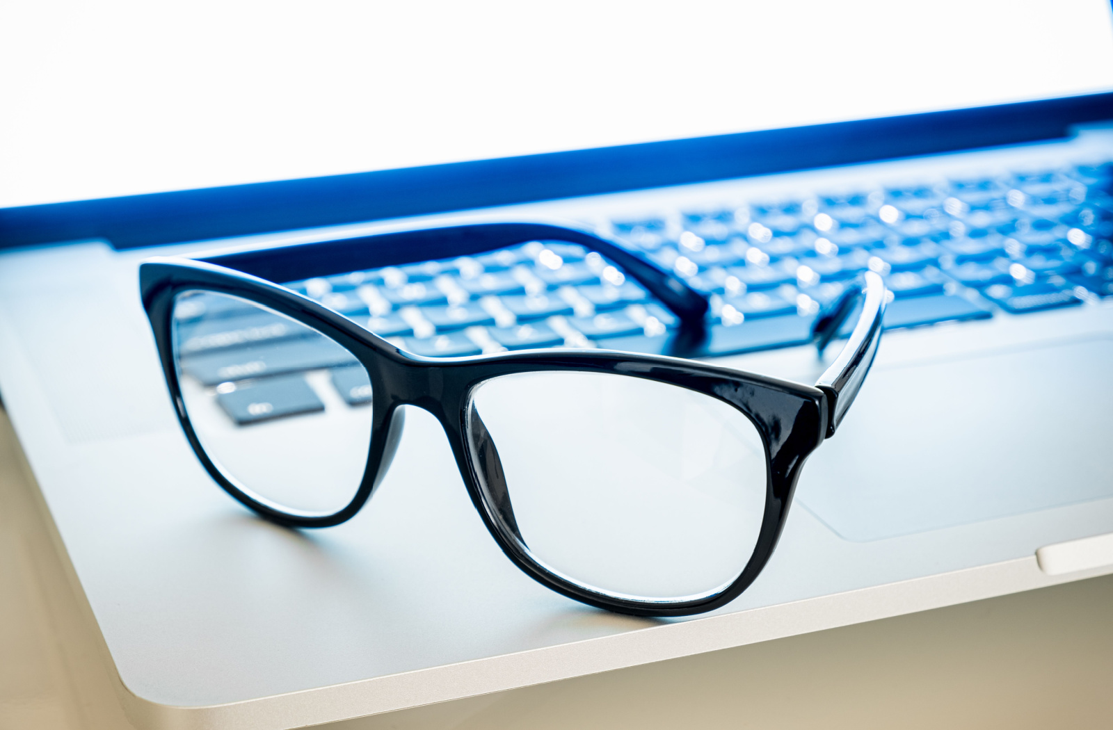 A pair of blue light glasses on an open laptop.