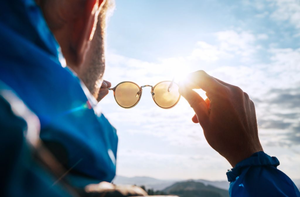 man holding sunglasses up to the sun.