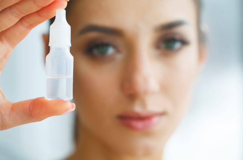 A close-up image of a young adult holding up a bottle of eye drops to help with dry eye disease.