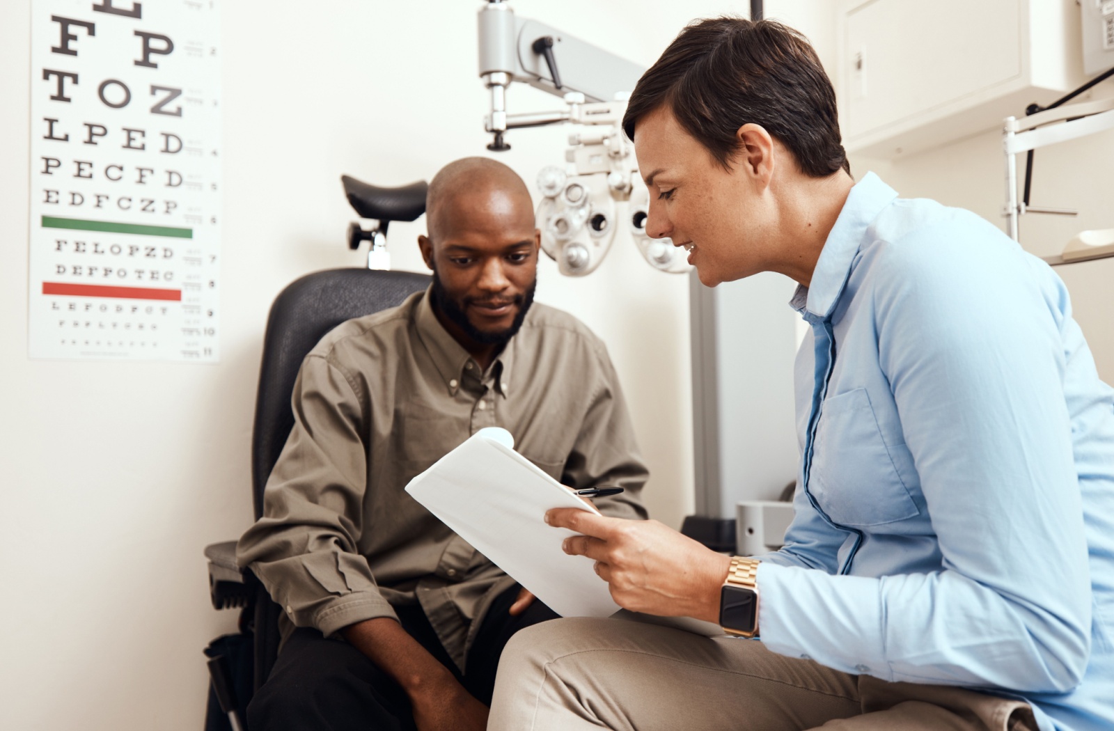 An optometrist showing a patient their clipboard after an eye exam and explaining their hereditary risk of developing glaucoma.