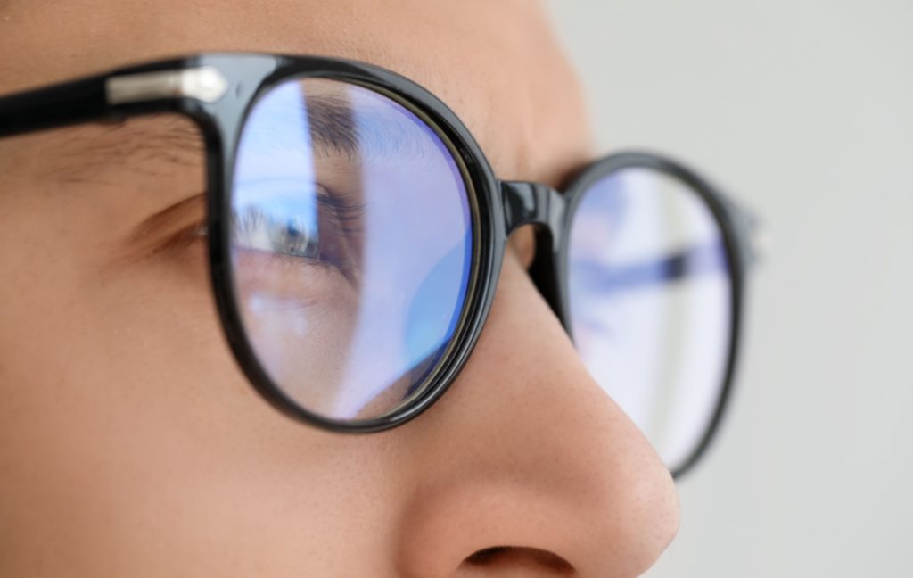 A person wearing glasses to correct their myopia looks off into the distance. The light from a window reflects of their glasses.