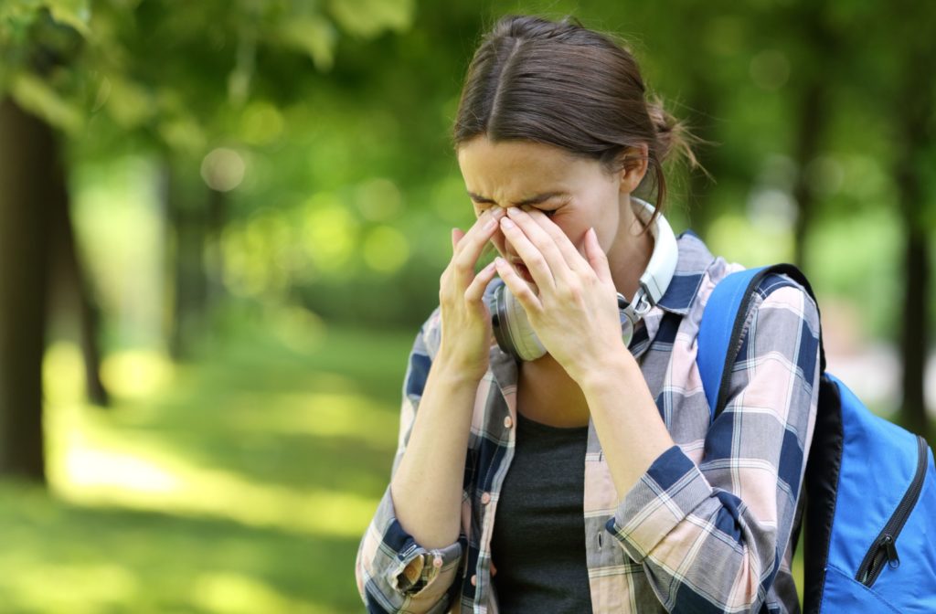 A person walking outside, rubbing their eyes from allergies.