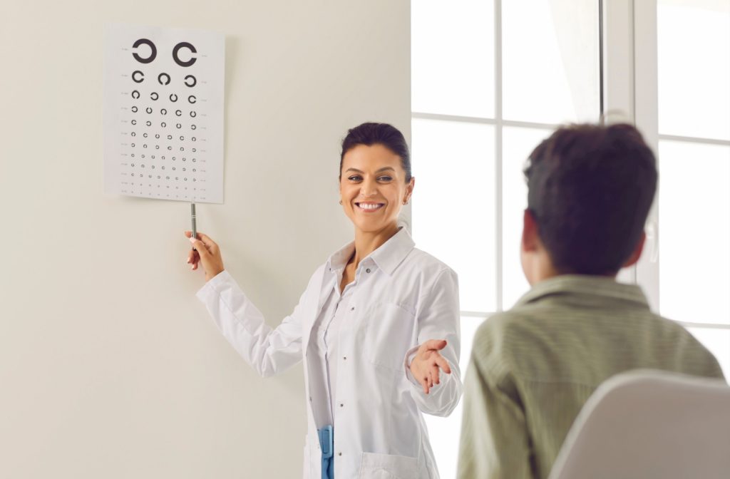 An optometrist smiles while pointing to an eye chart during a vision test with a child sitting across from them.