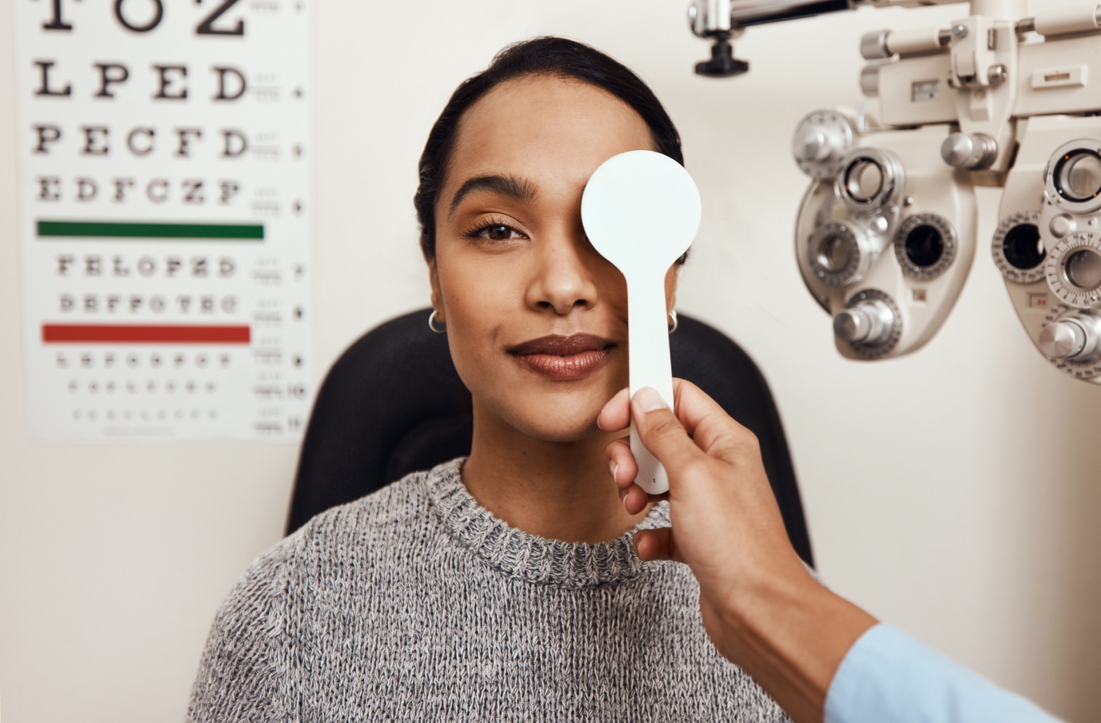 Optometrist covering one eye of a female patient during a vision test at an eye exam in Calgary.