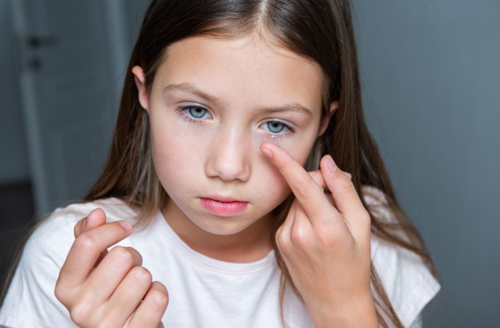 Young girl putting in a contact lens into her left eye.