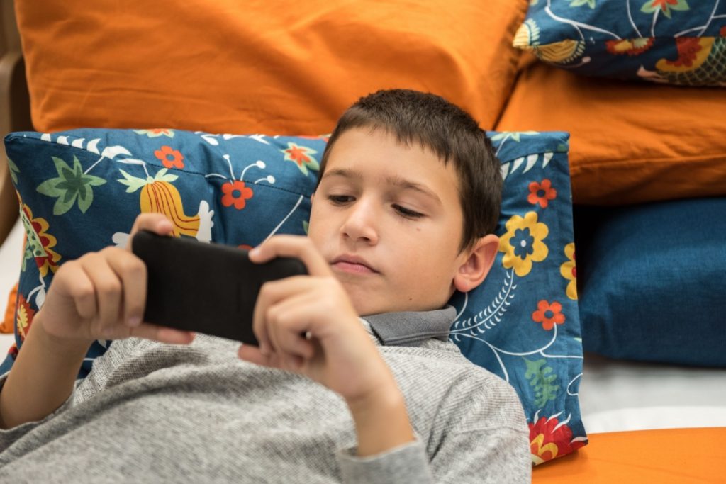 Teen boy laying while using his phone.