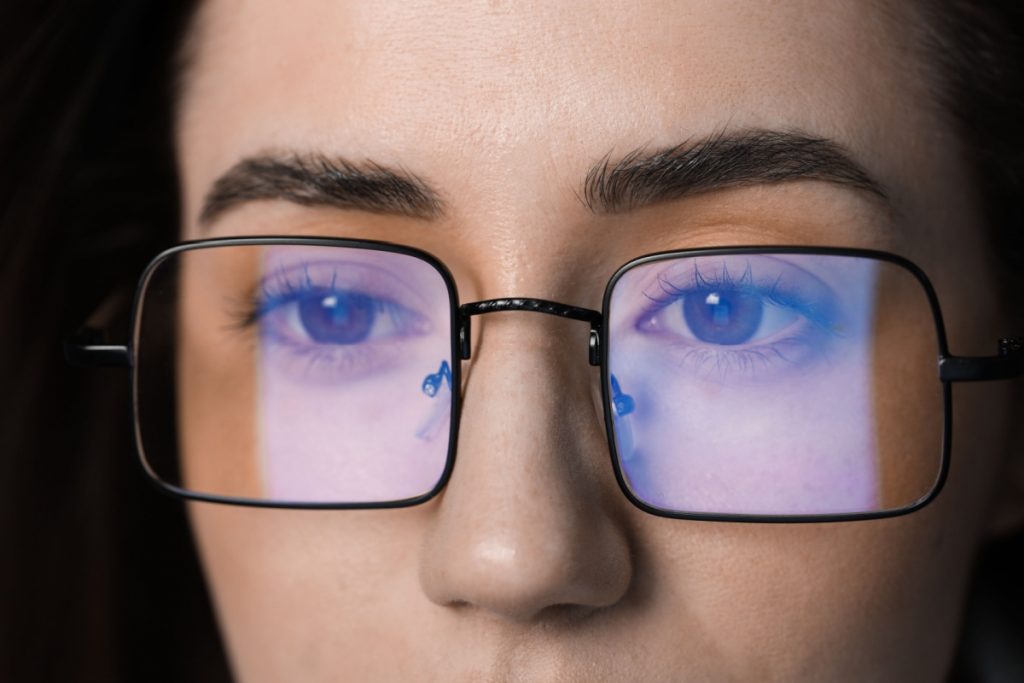 Up close image of blue light reflecting off of a woman's glasses.